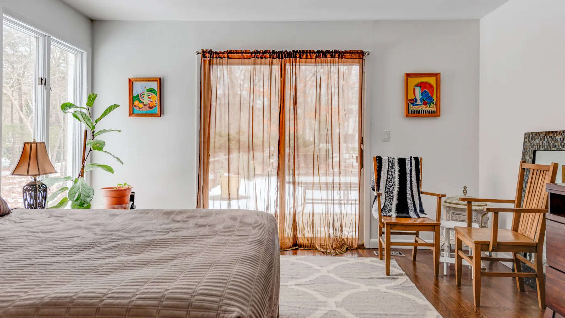 A bright bedroom with a bed, curtained windows, and wooden seating.