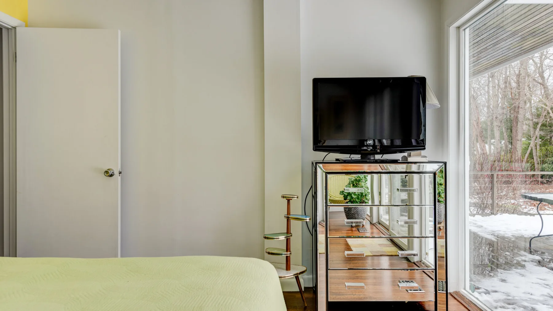 A bedroom with a bed, television, and a large window overlooking a snowy yard.