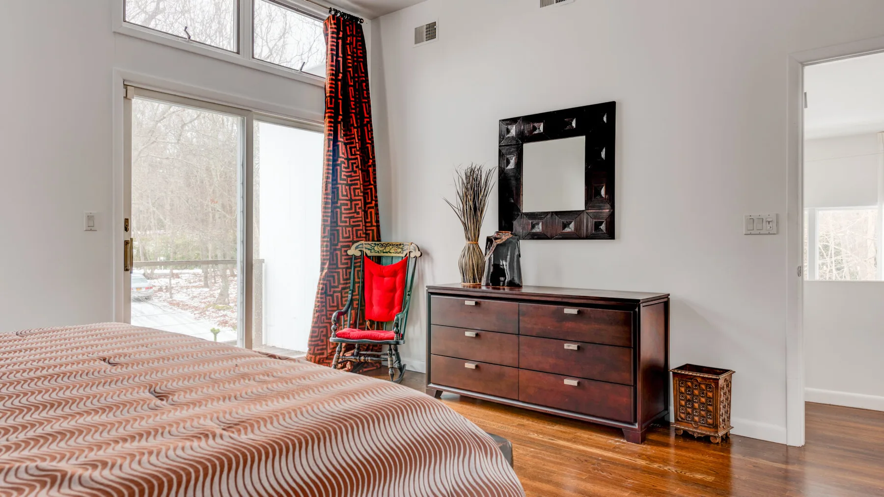 A bright bedroom with a patterned bedspread and a wooden dresser.