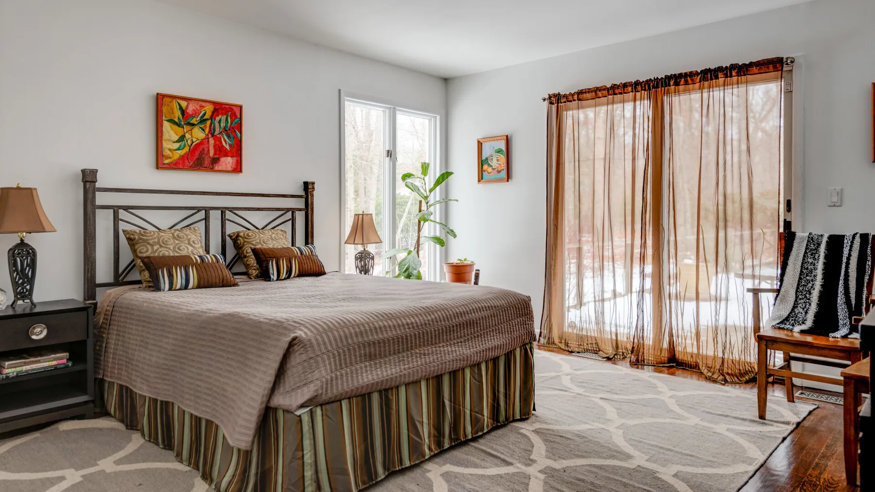 A bedroom with a large bed, colorful wall art, and curtains over a glass door.