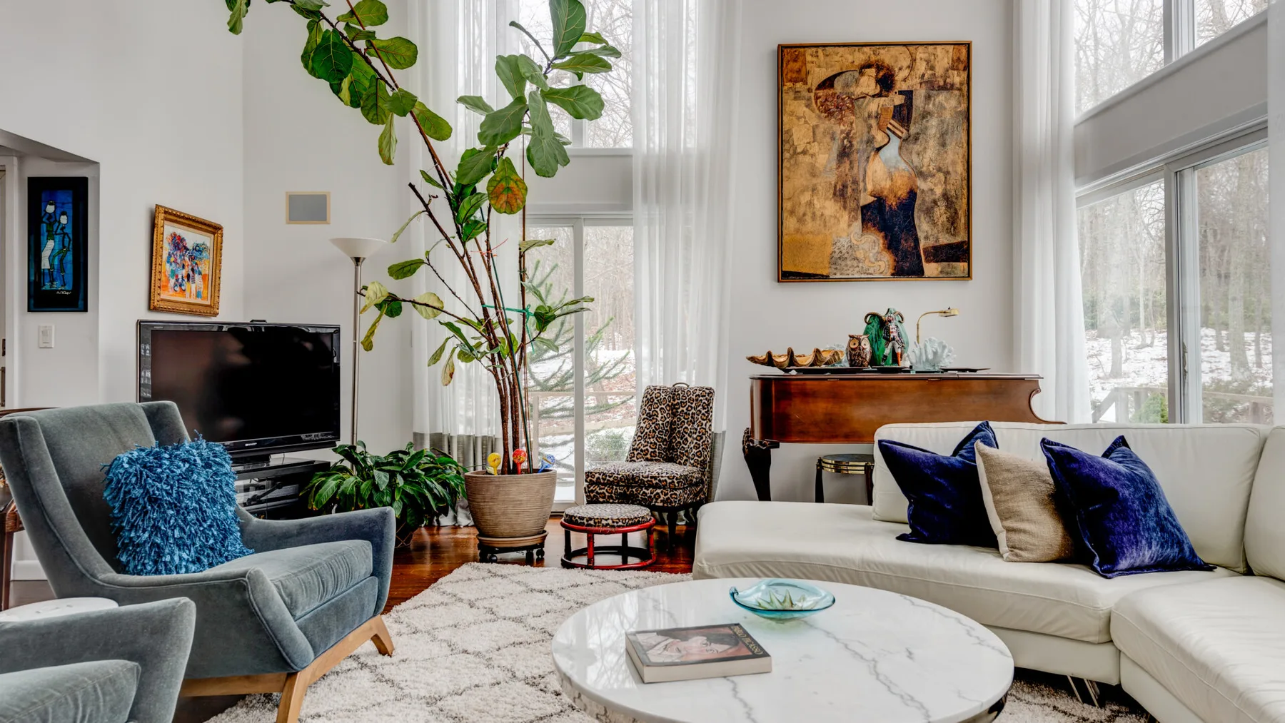 A bright living room with seating, large windows, and a potted plant.