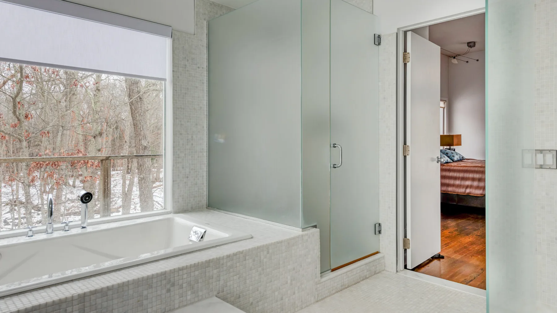 A bathroom with a bathtub beside a glass shower and a large window.