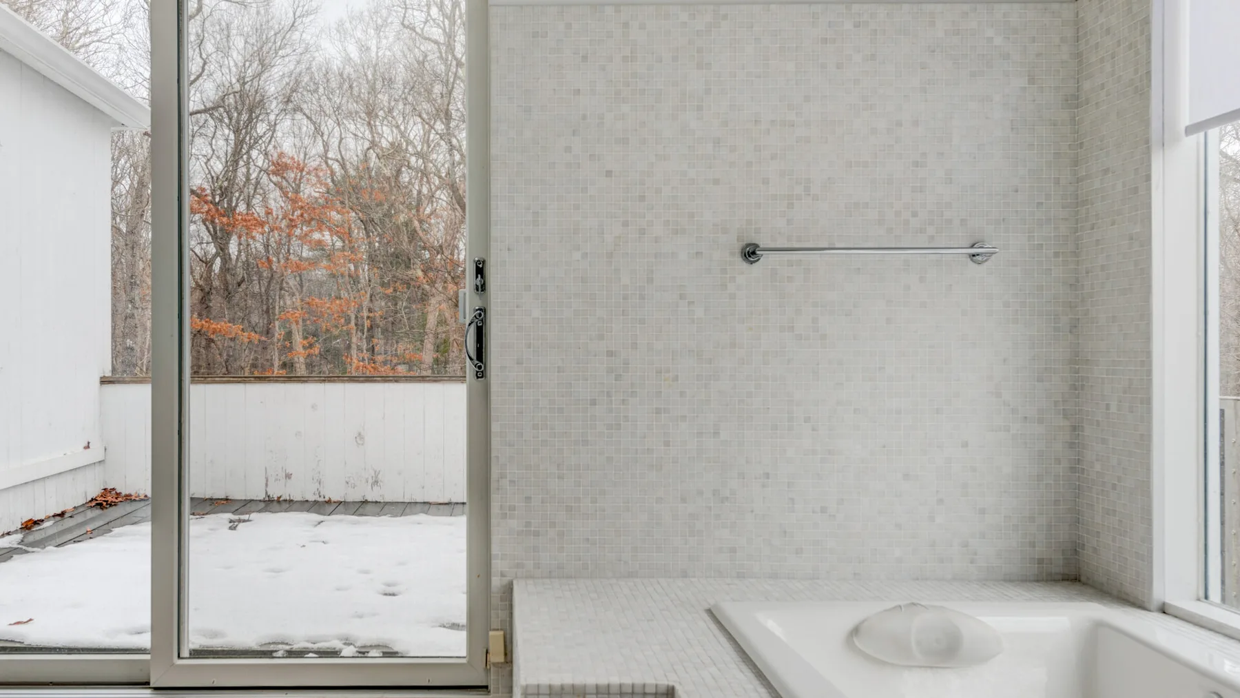 A bright bathroom with a bathtub beside a large window overlooking a snowy outdoor area.