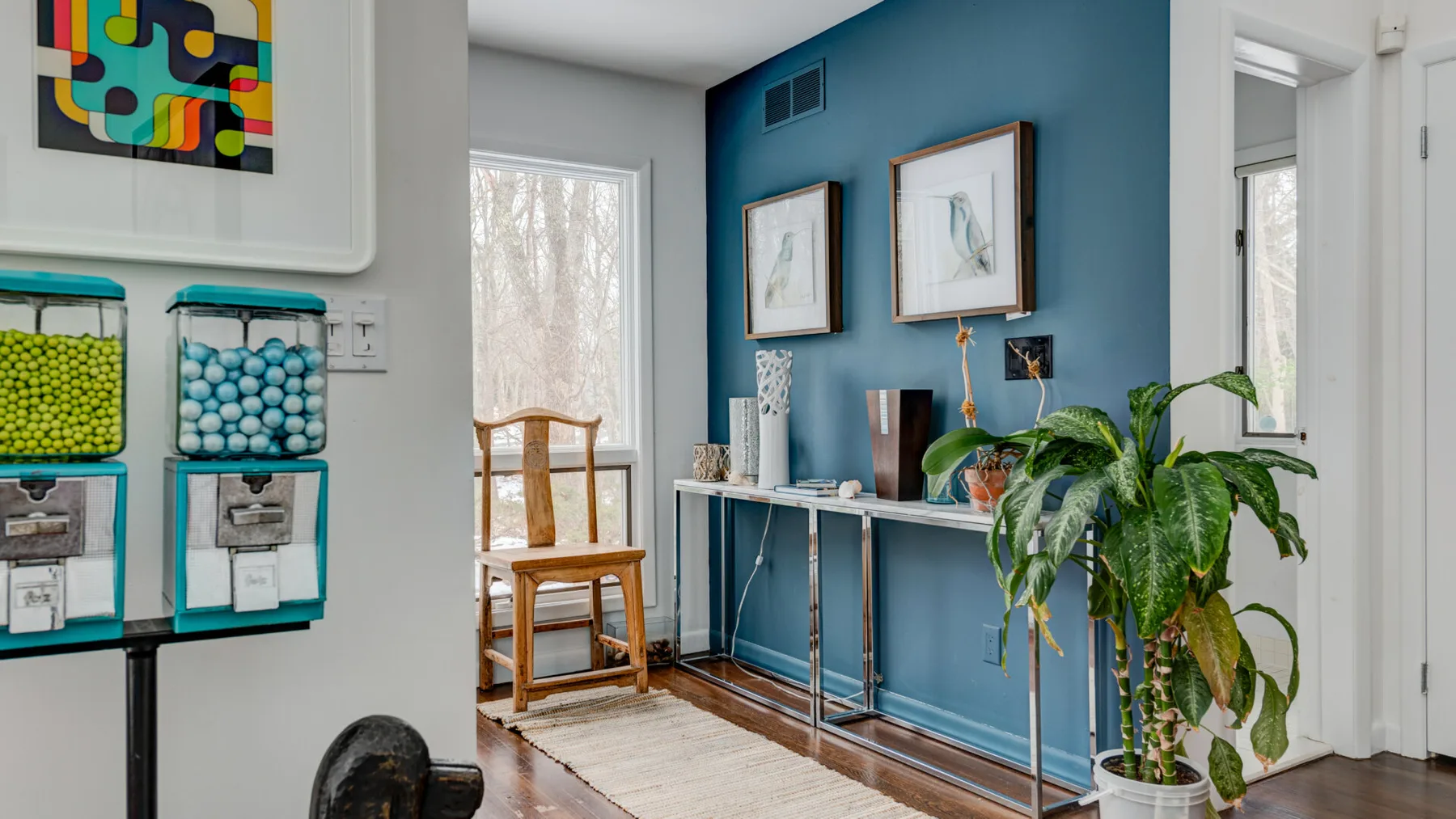 A colorful interior hallway with framed artwork, a console table, and potted plants.