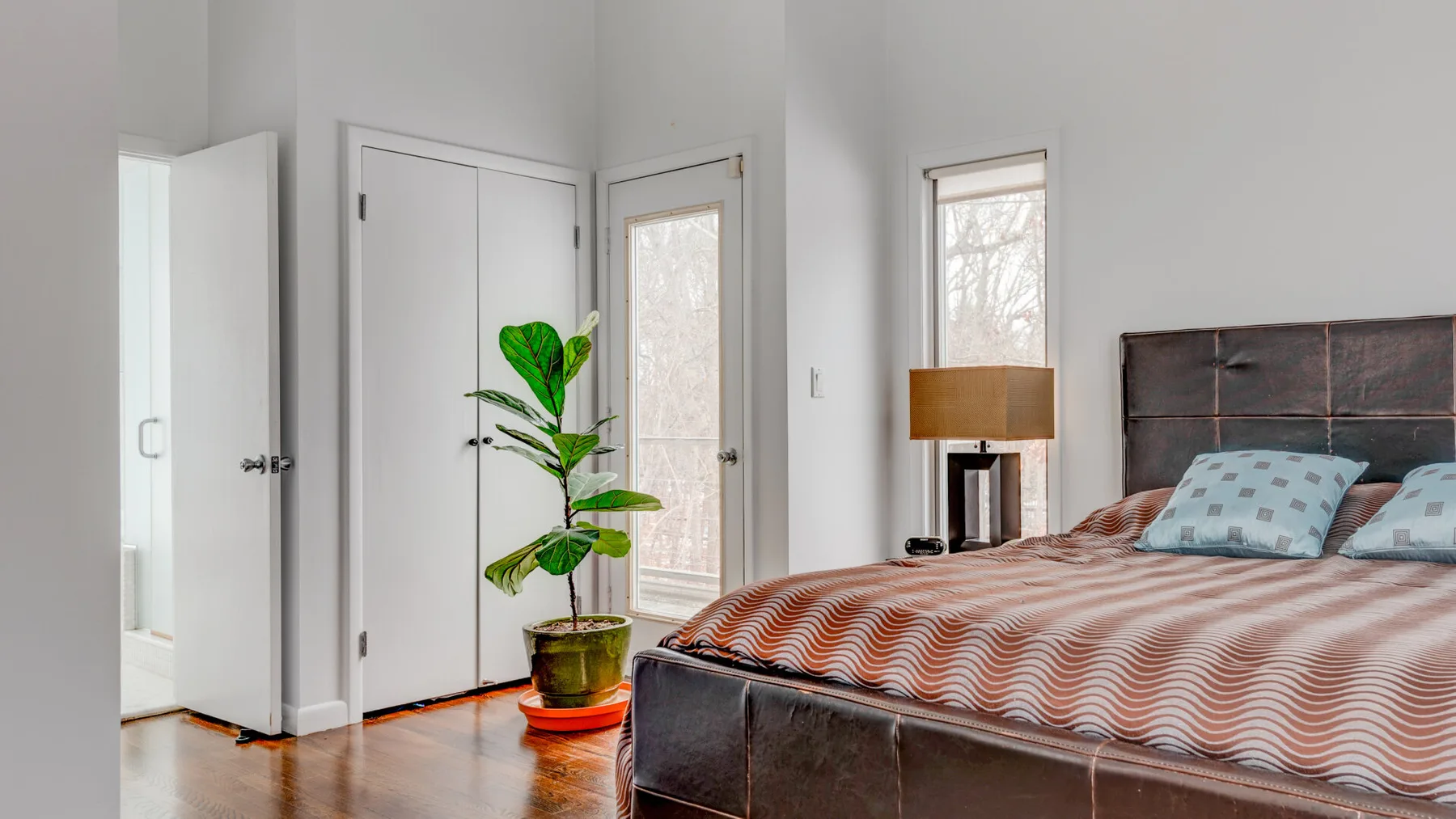 A bedroom with a bed and a potted plant beside the doors.