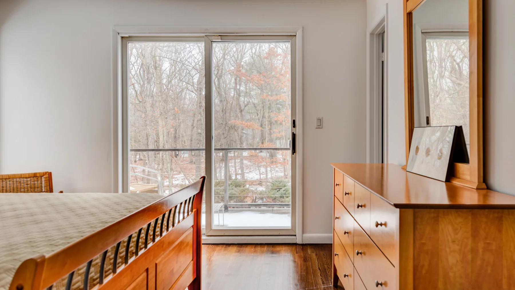 A bedroom with a wooden bed and dresser beside a large window.