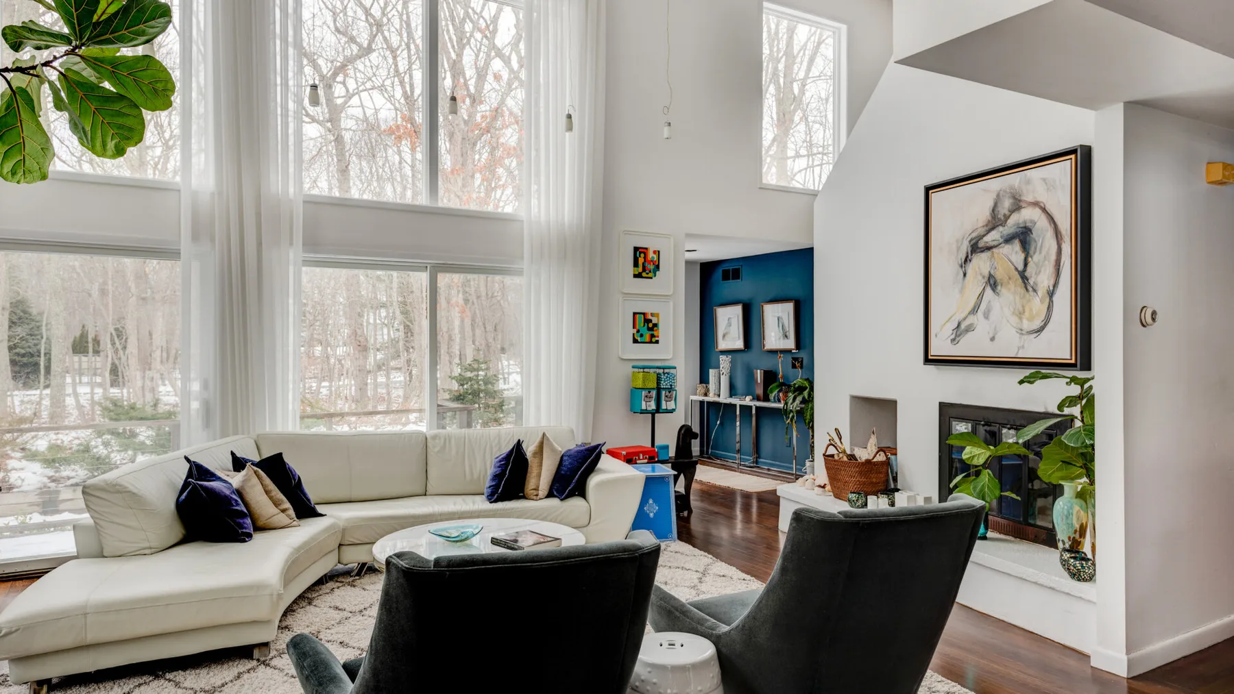 A bright living room with seating, large windows, and a framed artwork.