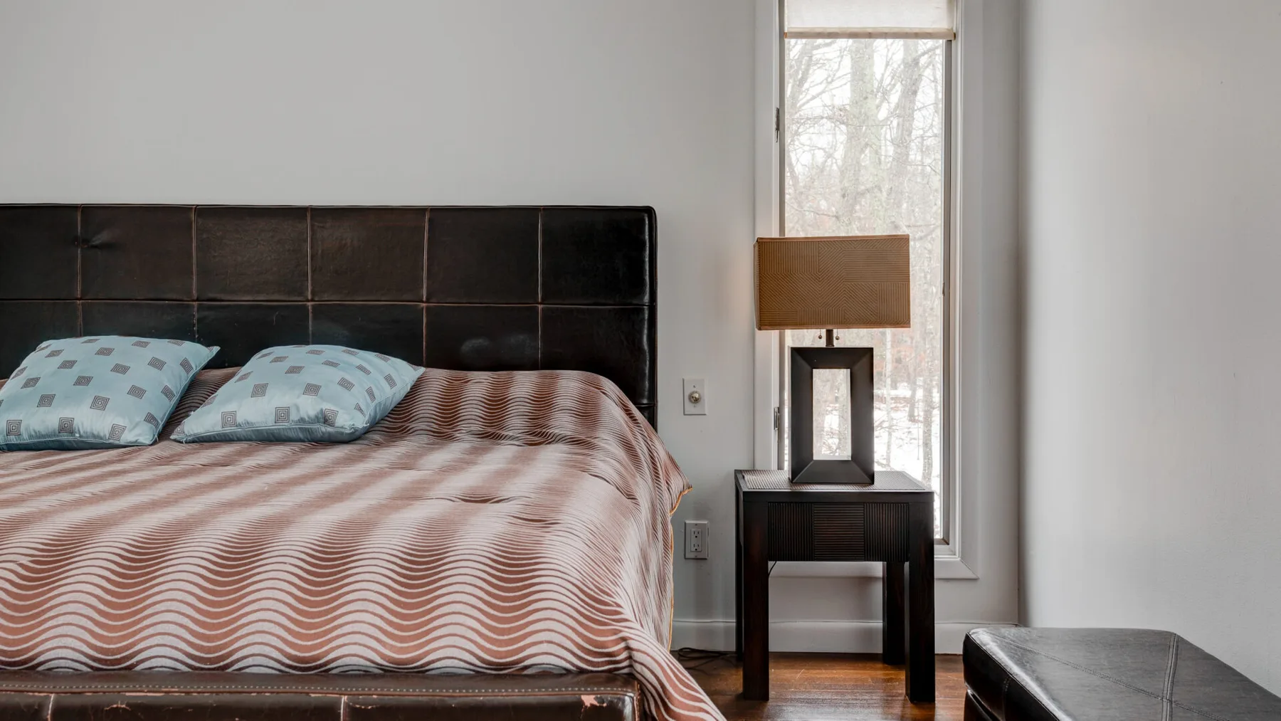 A bedroom with a bed beside a window and a small table.