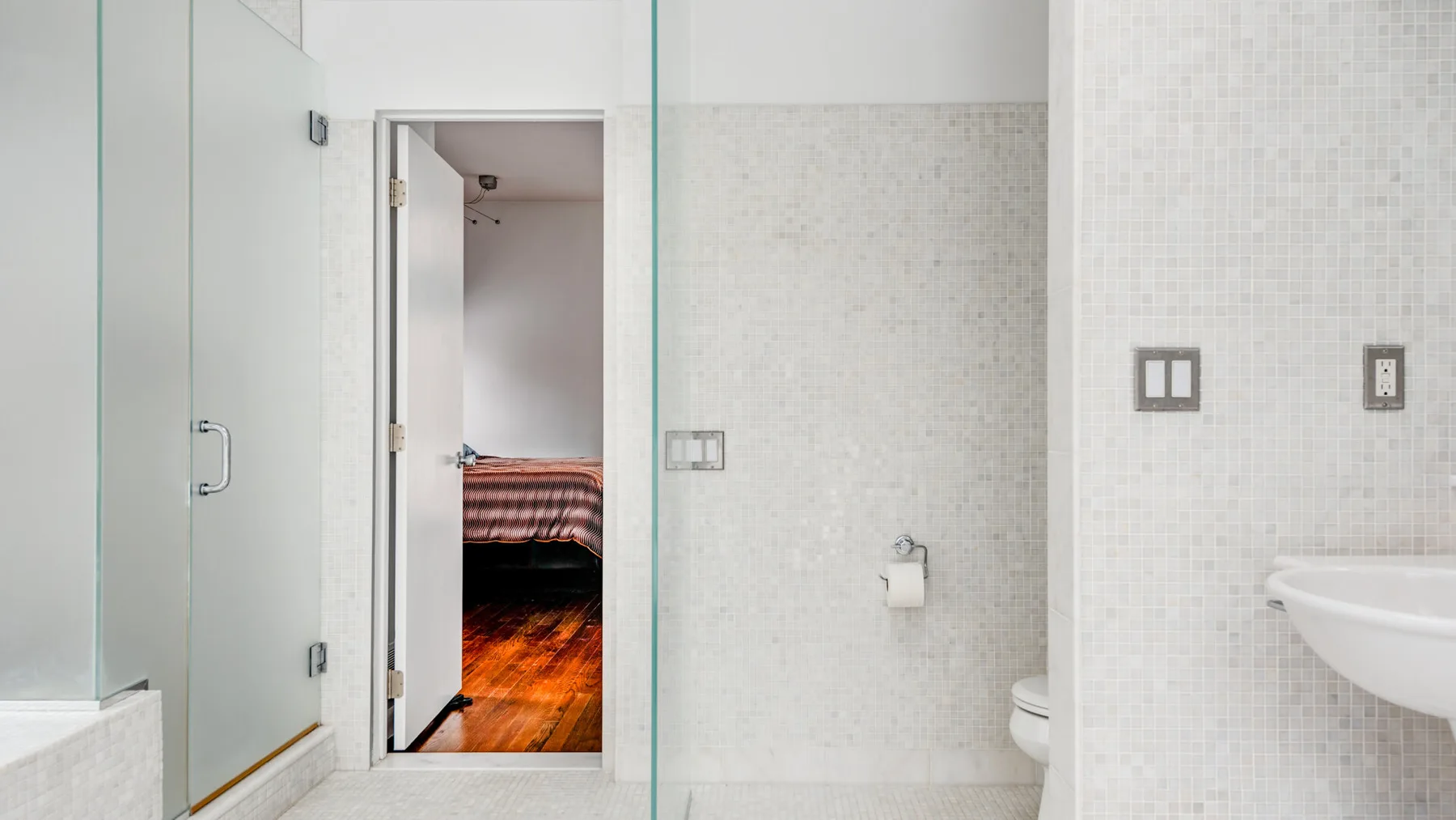 A tiled bathroom with a glass shower and a sink beside an open doorway.