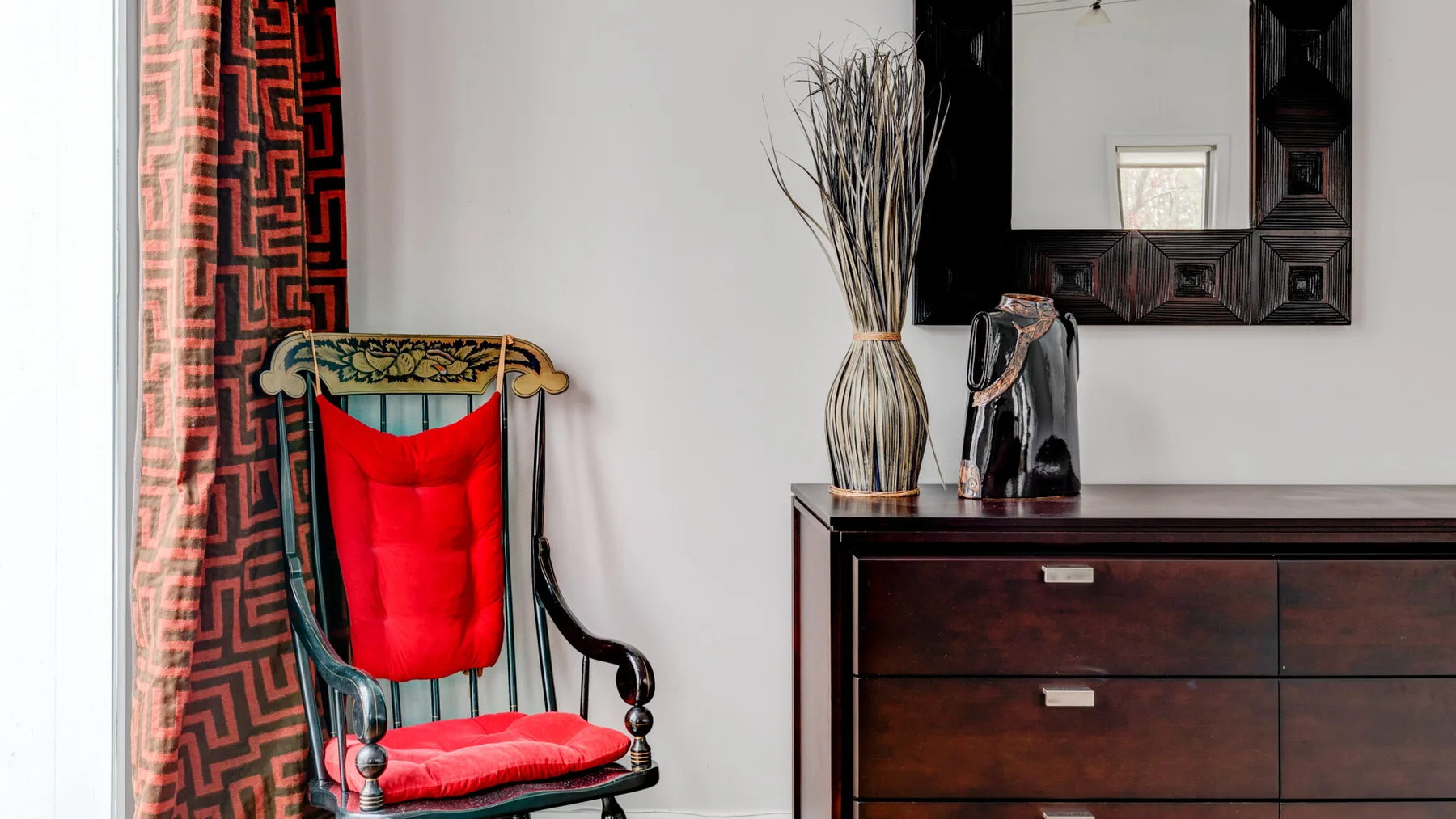 A furnished room corner with a red cushioned chair beside a dark dresser.