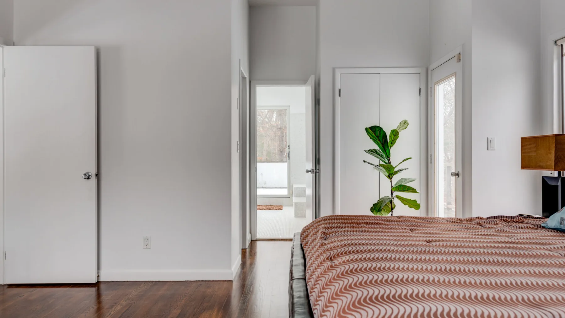 A bright bedroom with a patterned bedspread and a leafy plant.