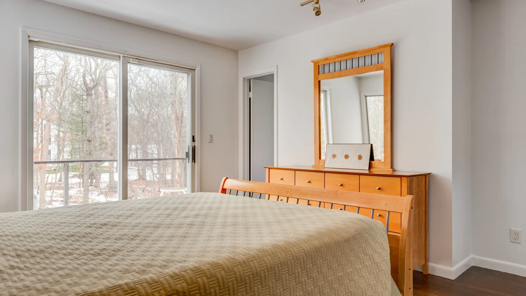 A bedroom with a bed beside a dresser and large windows.