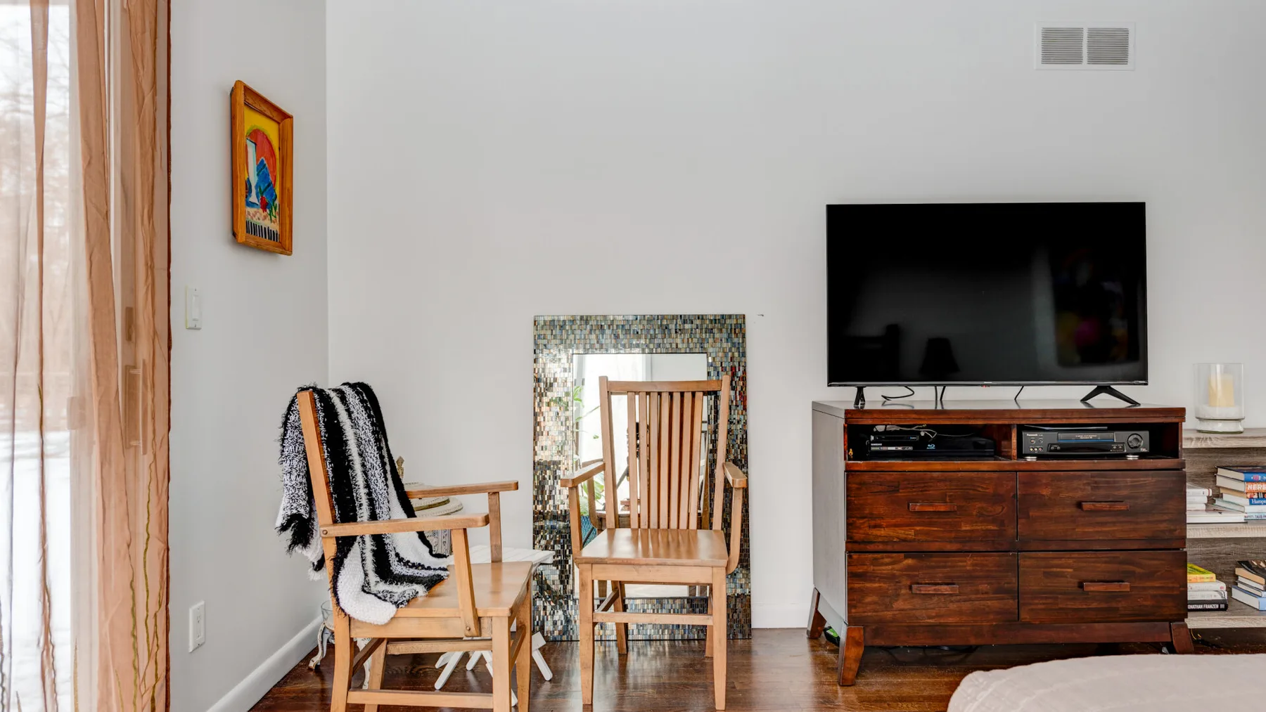 A bright living room with wooden seating and a television on a media cabinet.