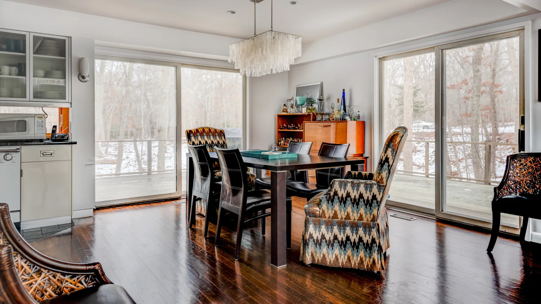 A dining area with a glass table and patterned seating beside large windows.