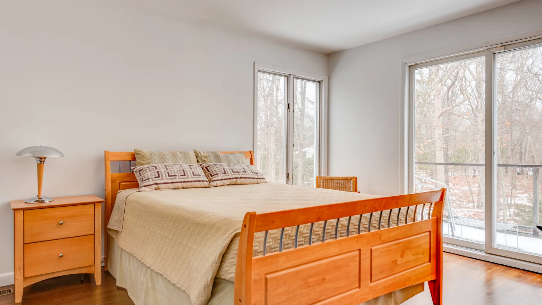 A bright bedroom with a wooden bed and large windows.