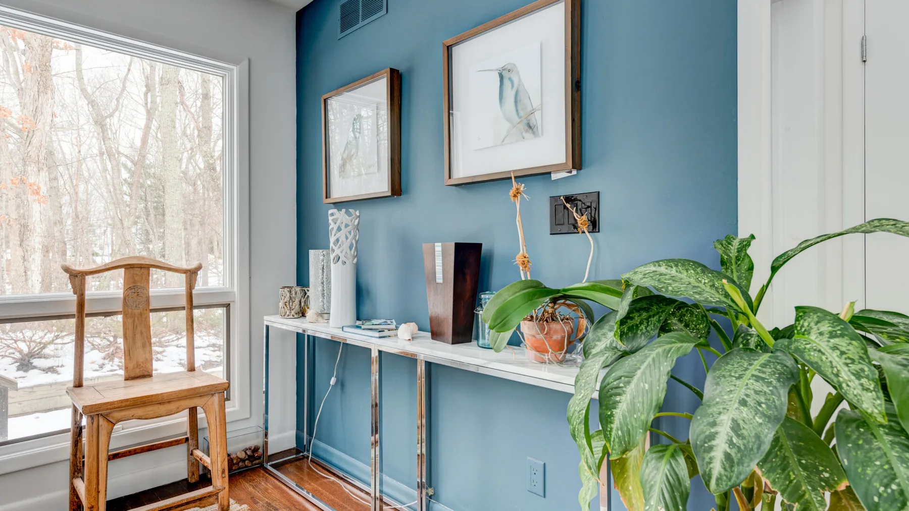 A blue-walled sitting area features framed art, a console table, and leafy plants.