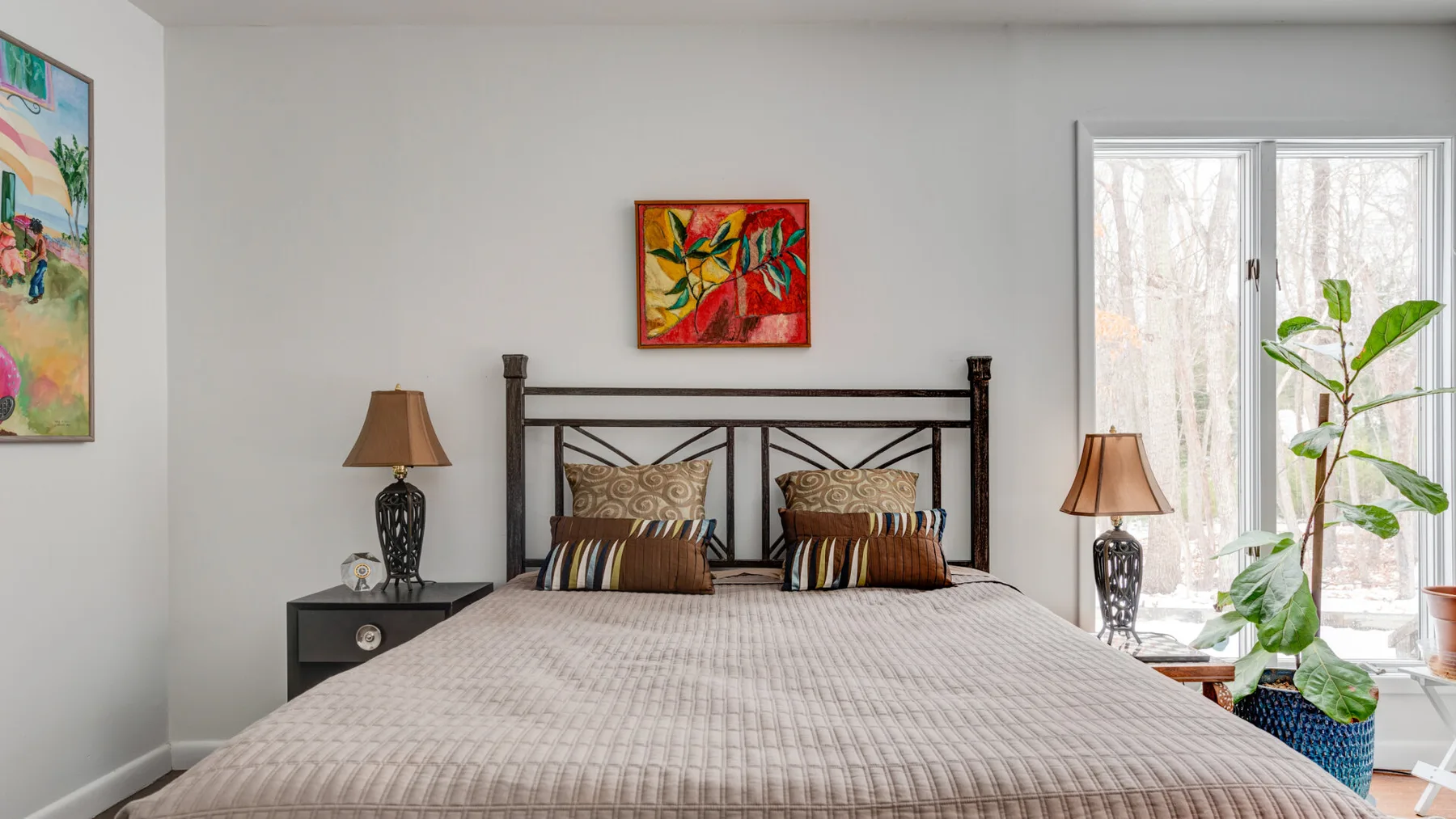 A bedroom with a neatly made bed, framed artwork, and a large window.
