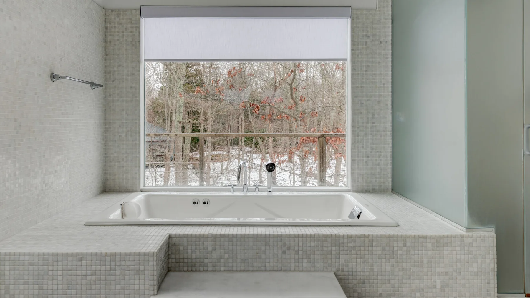 A tiled bathroom with a bathtub beneath a window overlooking trees.