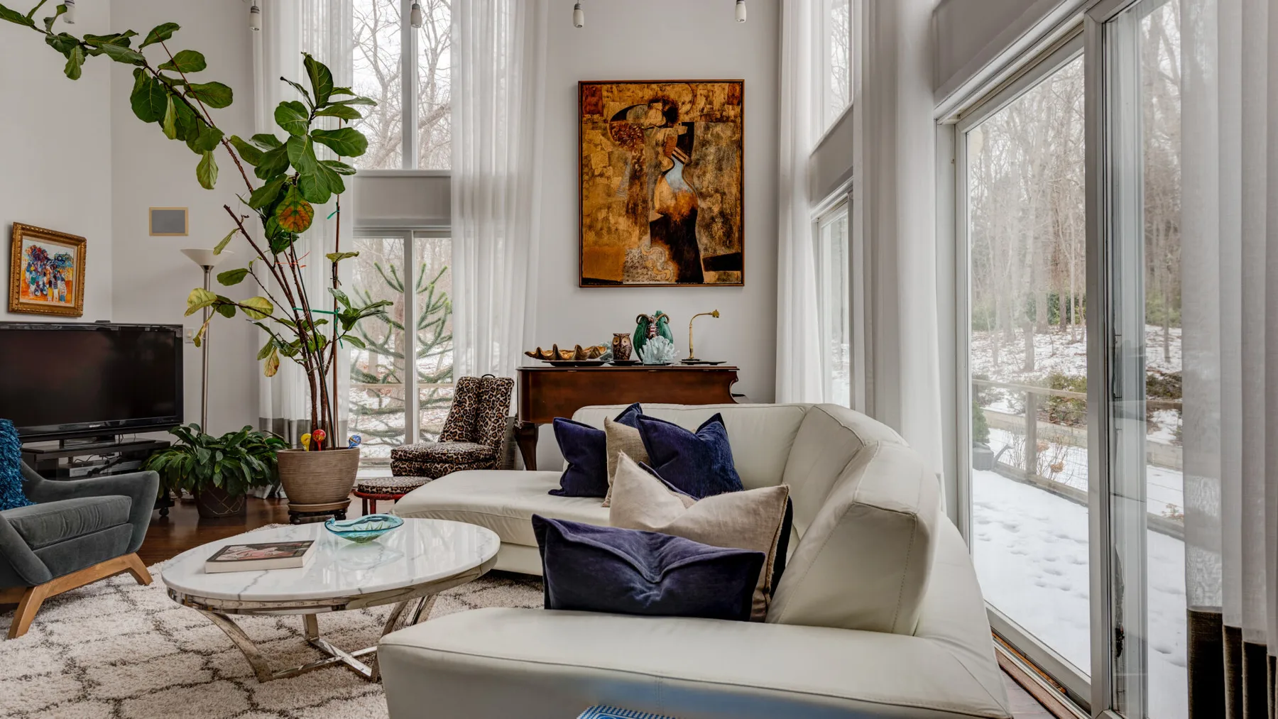 A bright living room with seating, a glass coffee table, and large windows.