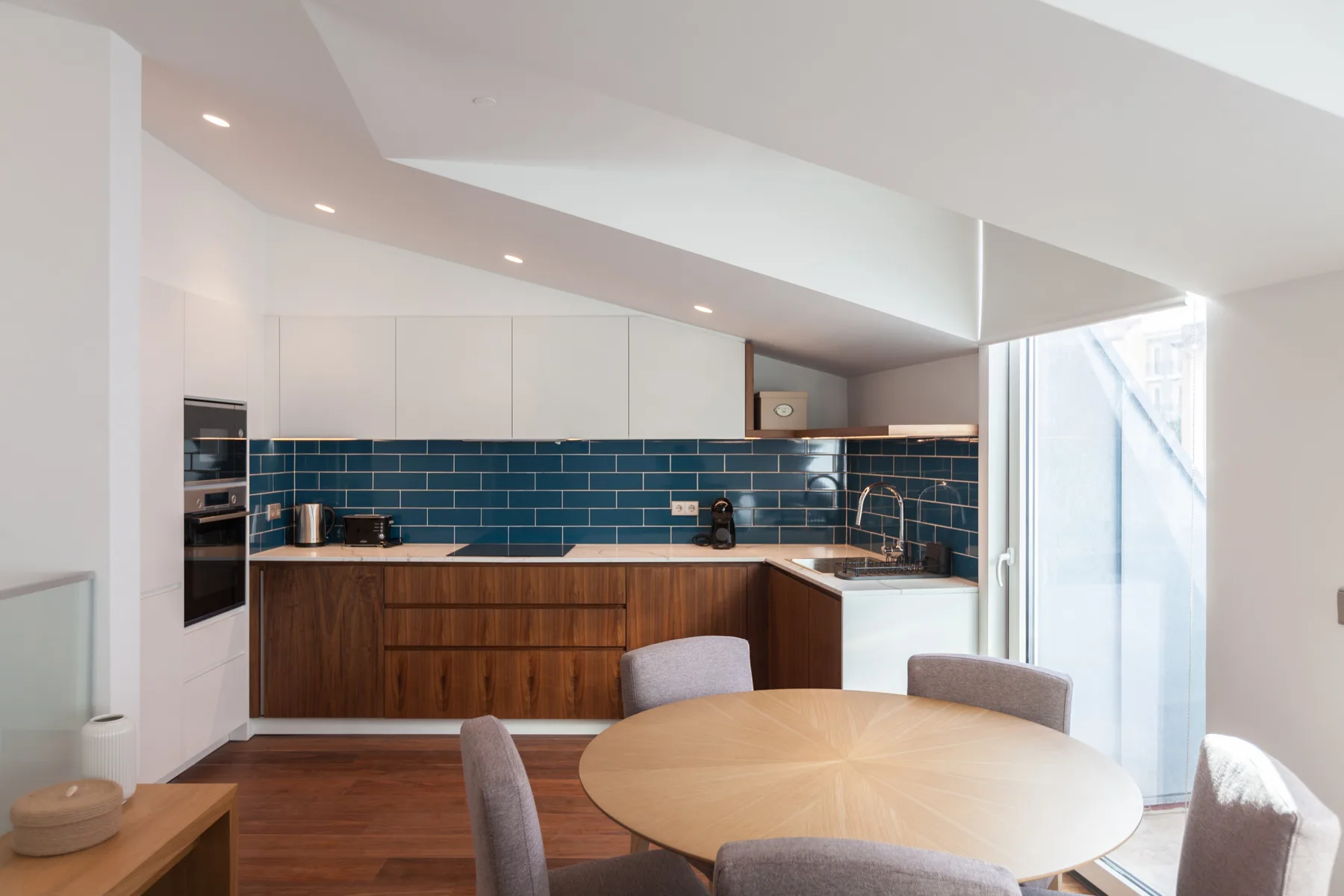Una cocina y comedor luminosos con azulejos azul oscuro y una mesa redonda.