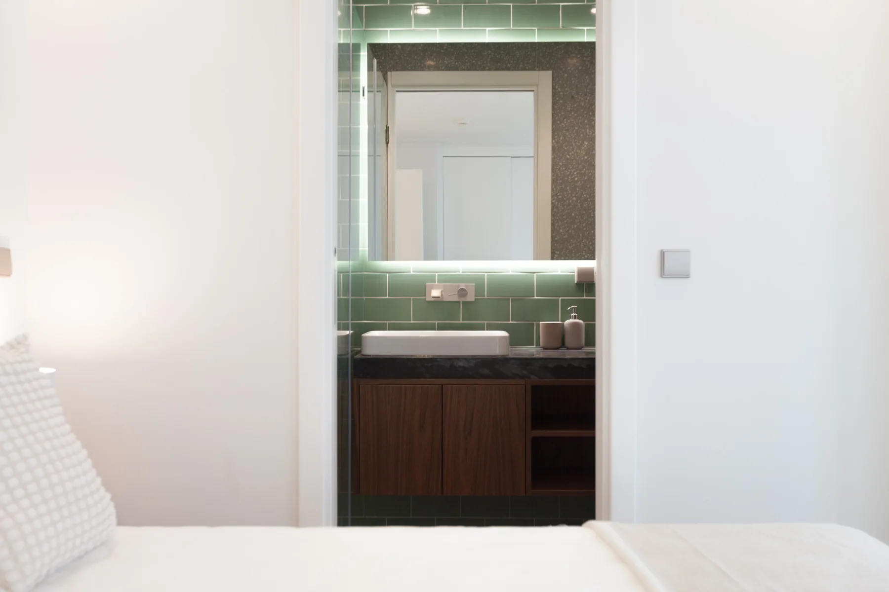 Se ve un lavabo de baño con espejo y azulejos verdes a través de la puerta.