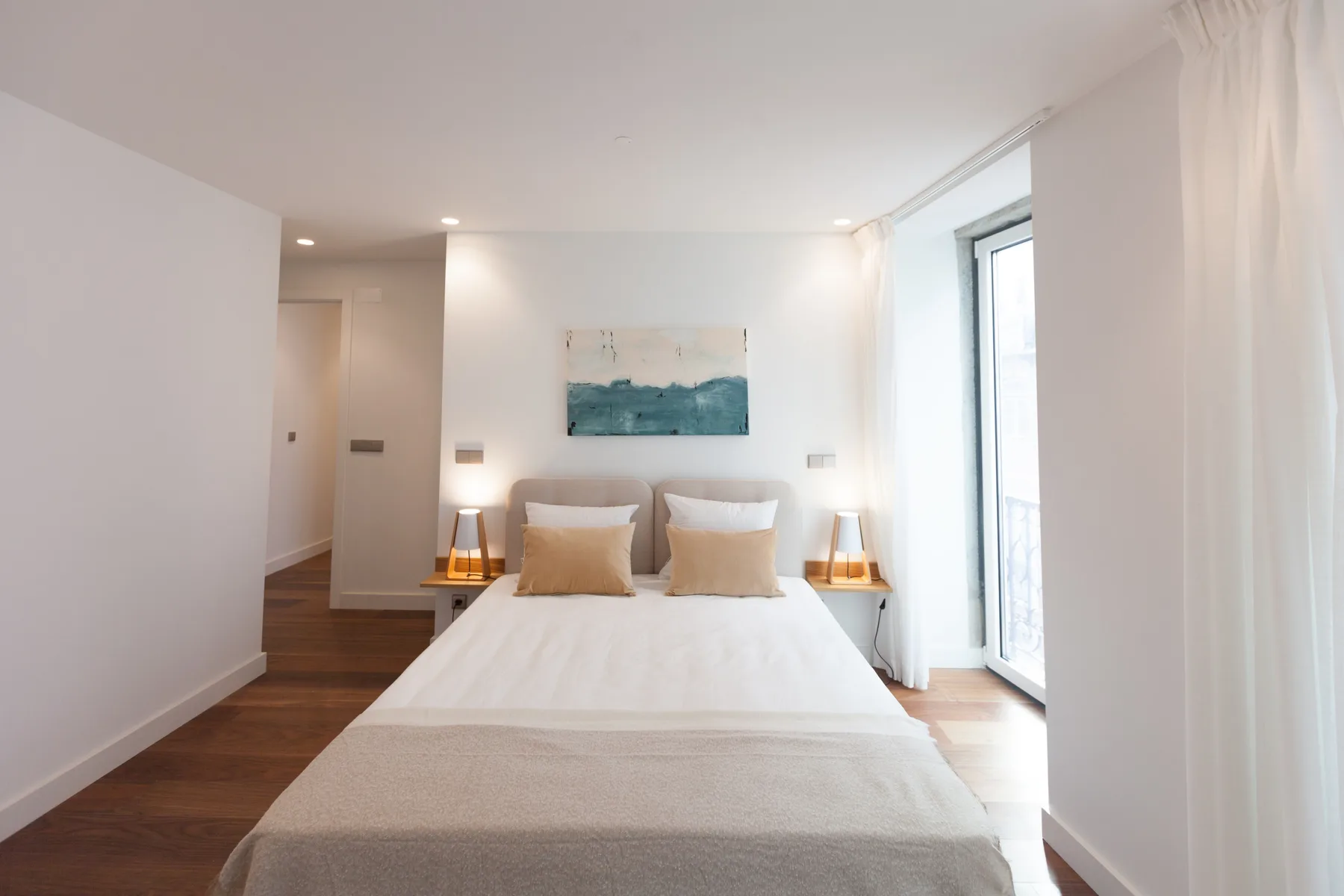 A bright bedroom with a bed, bedside tables, and a large window.