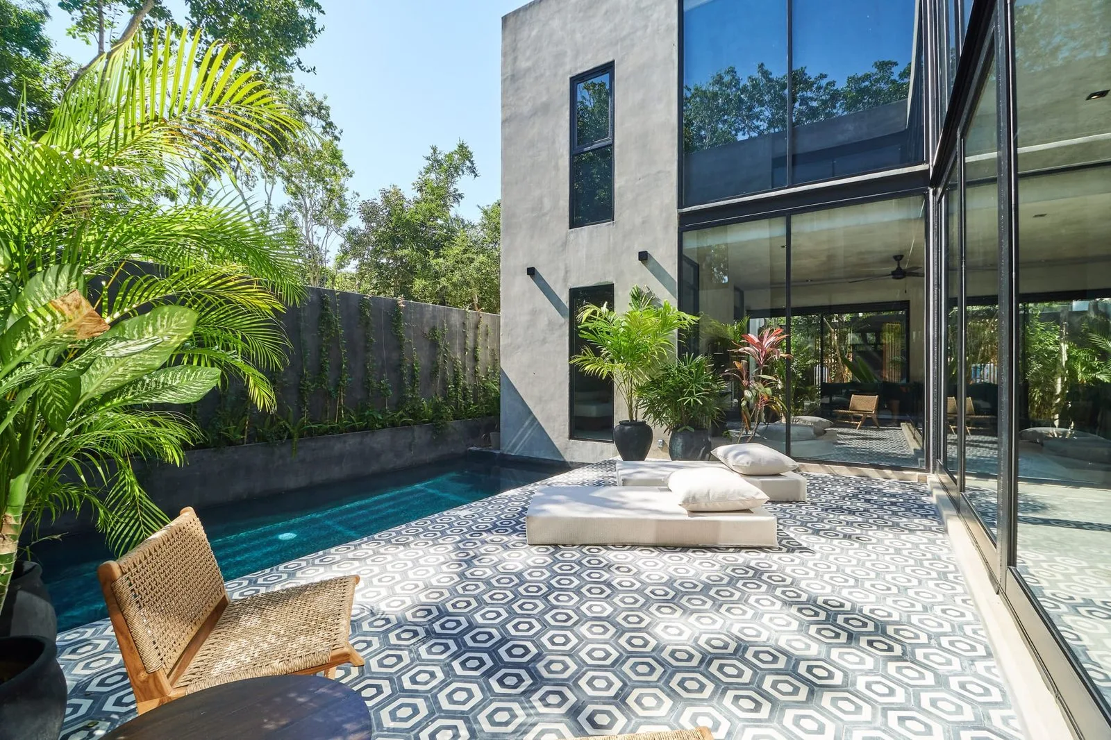 A tiled outdoor patio beside a narrow pool, with lounge seating and plants.
