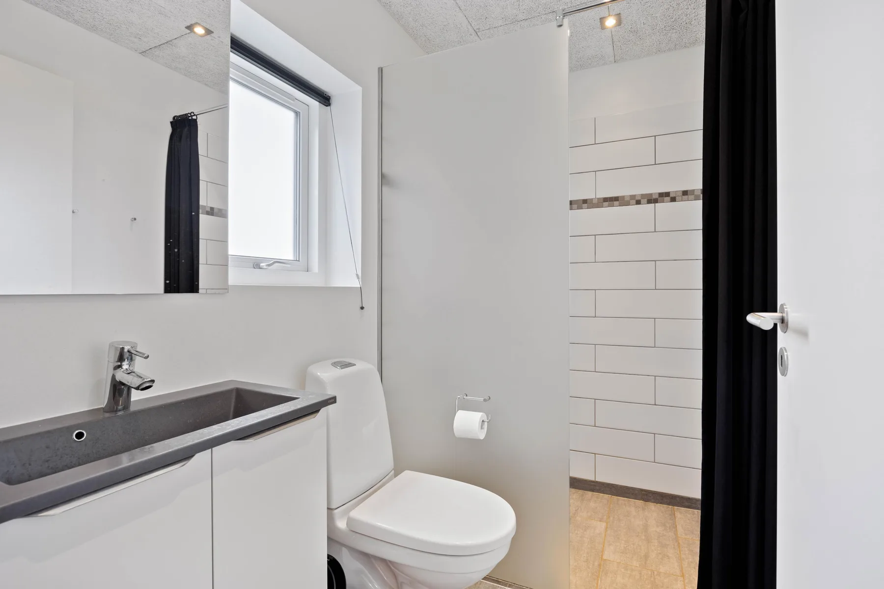 Baño luminoso con lavabo, inodoro y una zona de ducha con azulejos.