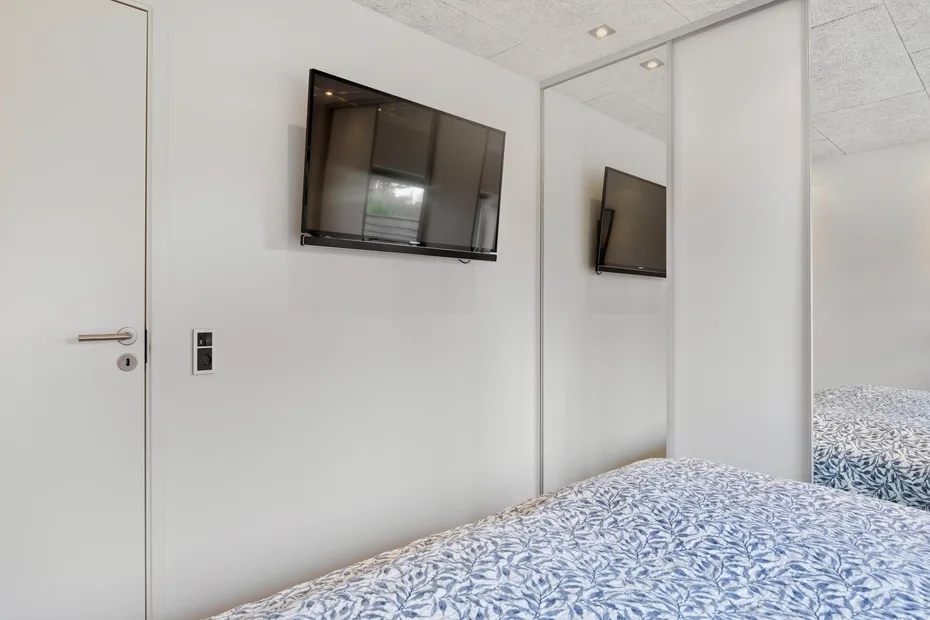 Un dormitorio con un televisor montado en la pared junto a la cama.