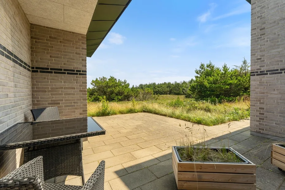 Un patio exterior pavimentado con asientos y jardineras da a un paisaje de hierba.