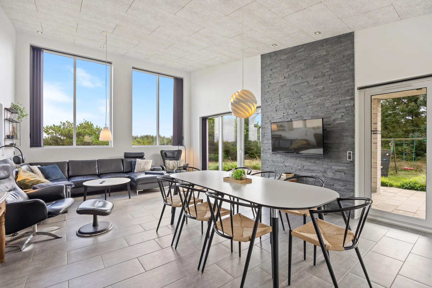 Una luminosa sala de estar y comedor con una mesa grande y asientos junto a ventanas altas.