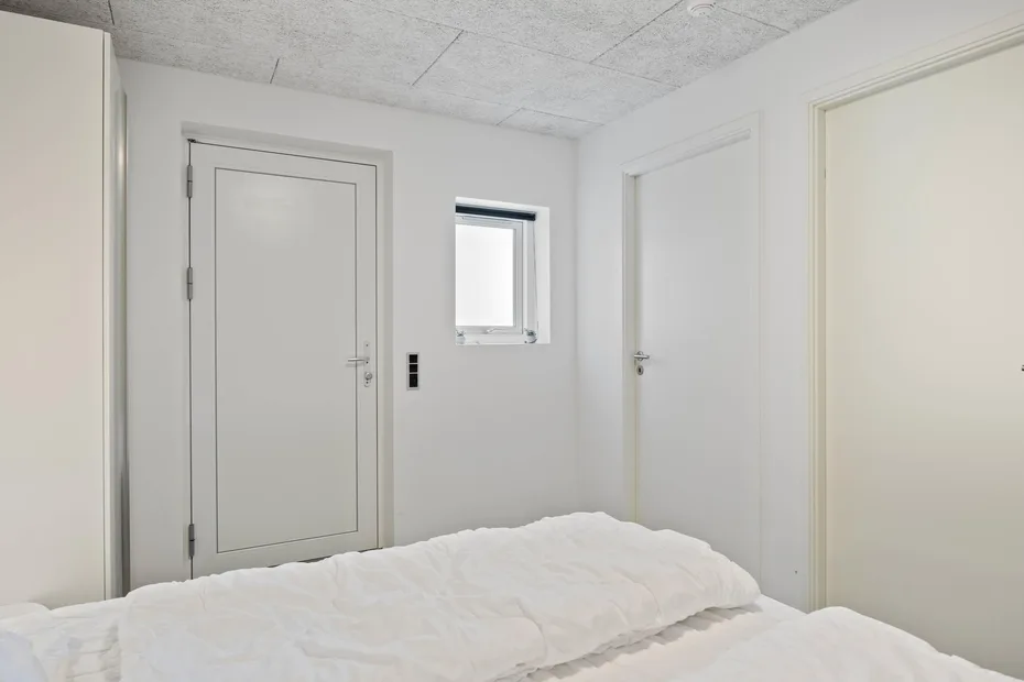 Un dormitorio con una cama blanca y varias puertas.