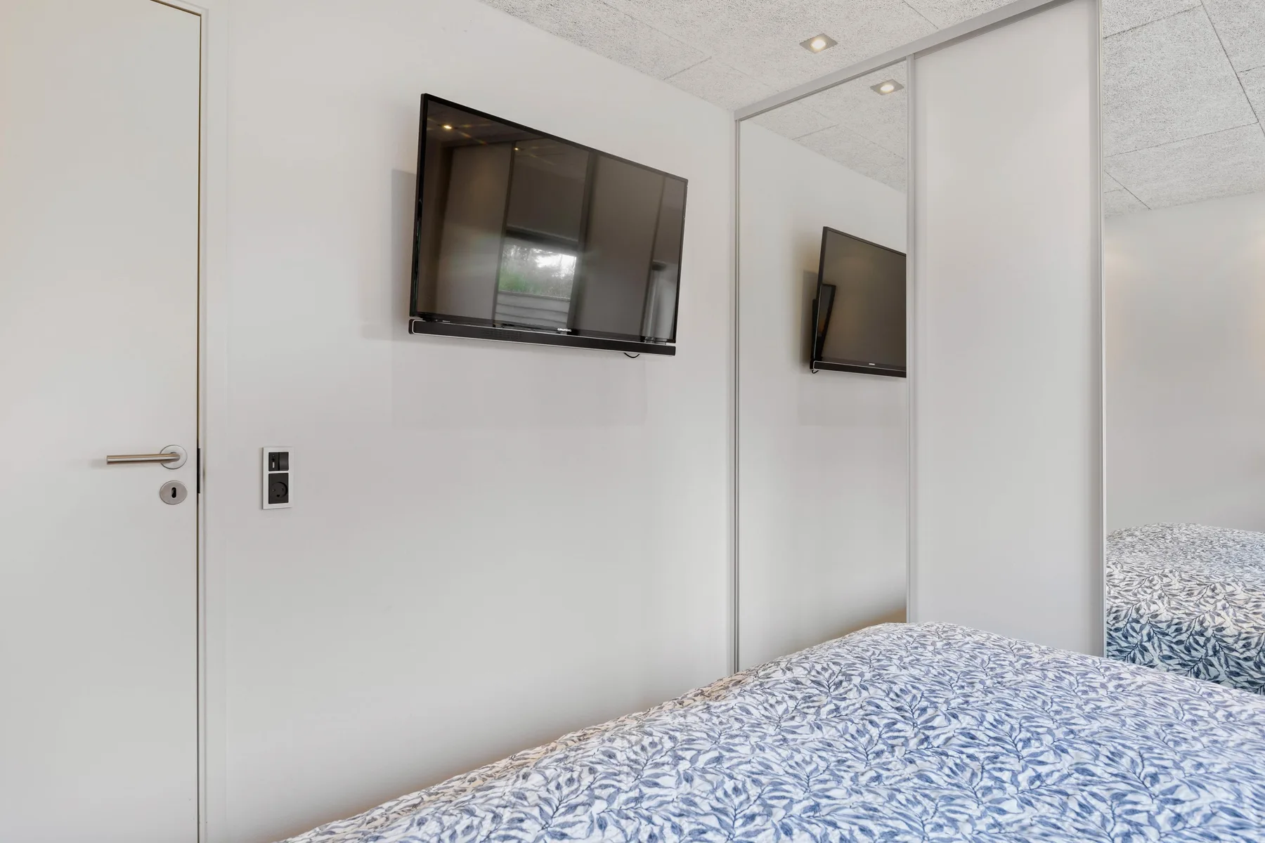 Dormitorio con ropa de cama estampada y un televisor montado en la pared.