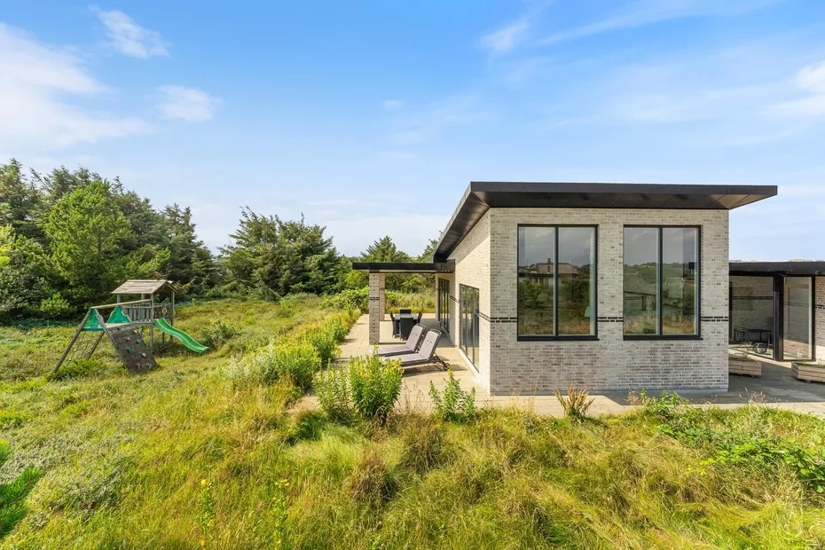 Una casa moderna está junto a un jardín de césped con una pequeña estructura de juegos.