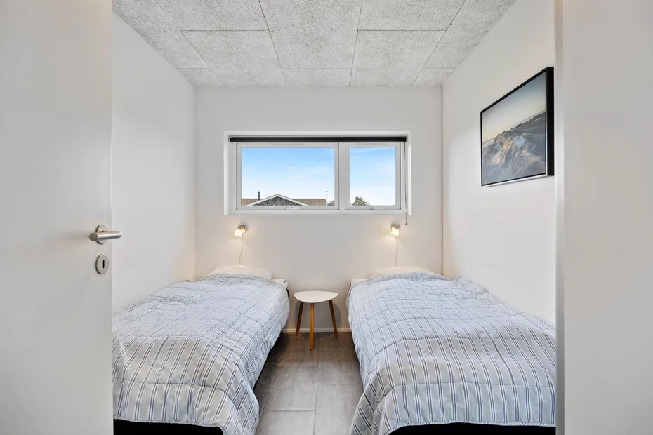 Un dormitorio luminoso con dos camas, una mesita y una ventana.