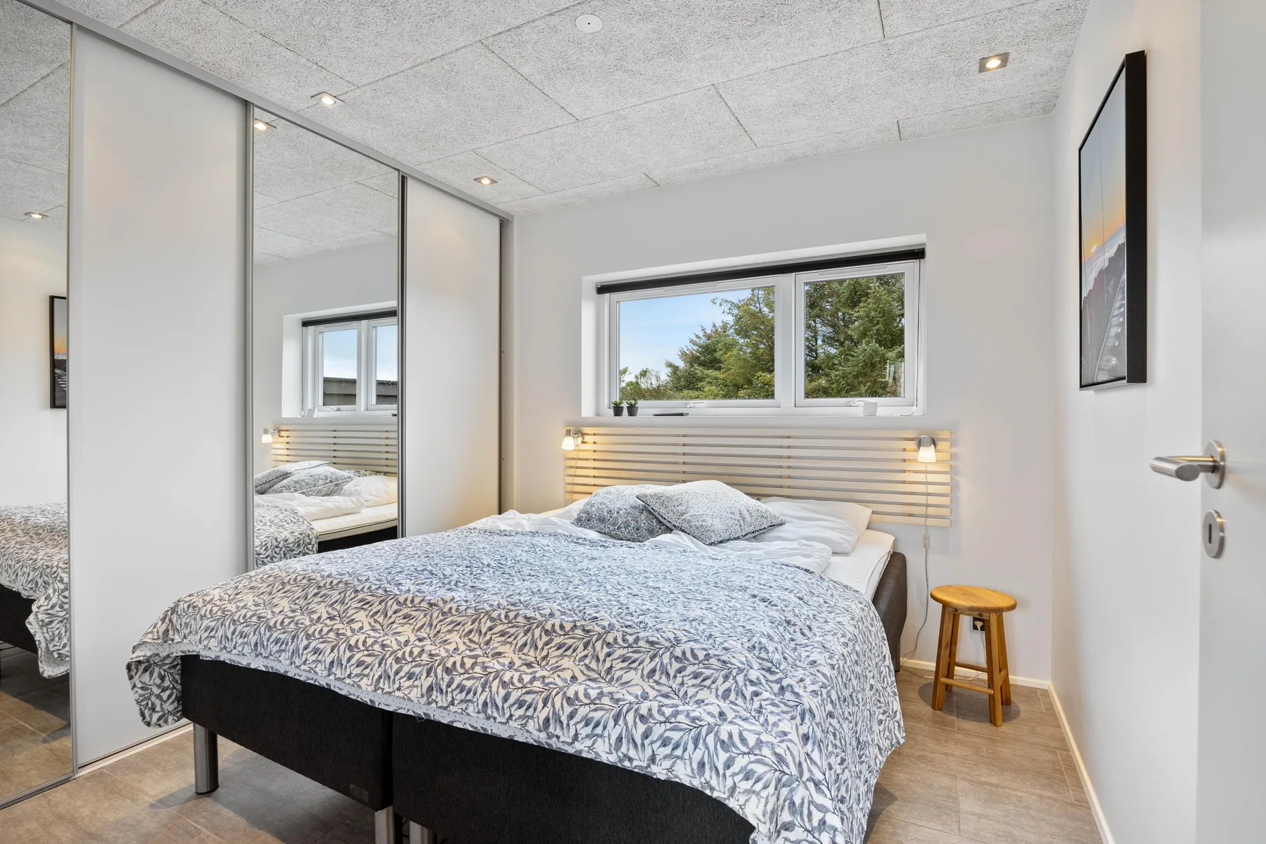 Un dormitorio con una cama bajo una ventana con vistas a los árboles.
