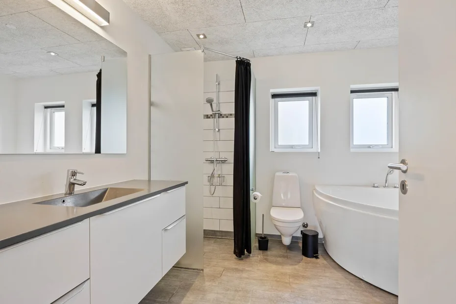 Un baño luminoso con un tocador largo, ducha, inodoro y bañera.