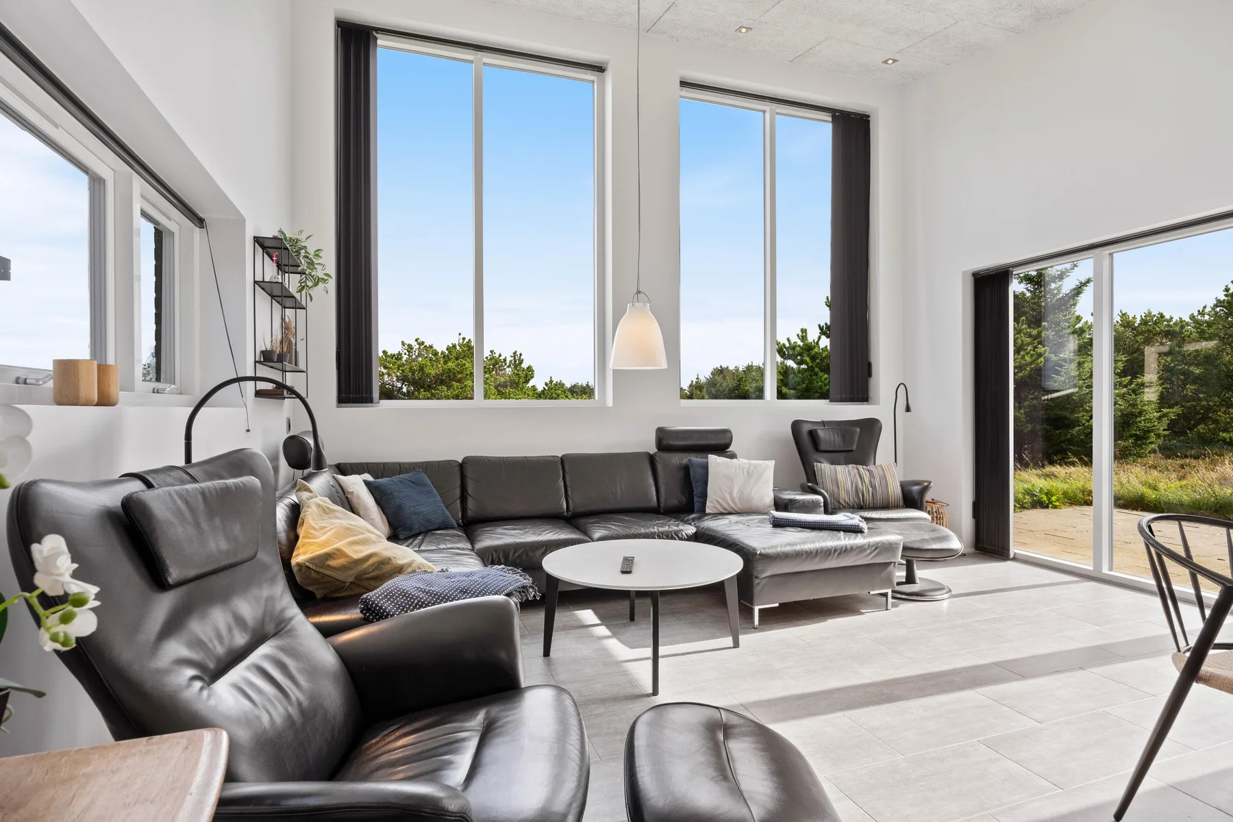 Una sala de estar luminosa con asientos alrededor de una mesa de centro y grandes ventanas.