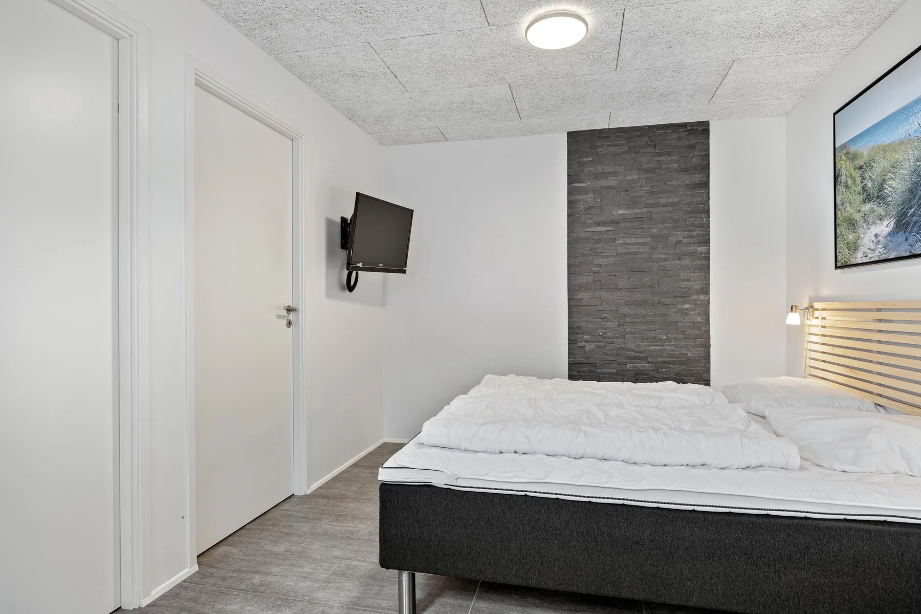 Dormitorio con una cama, un televisor montado en la pared y un panel oscuro.