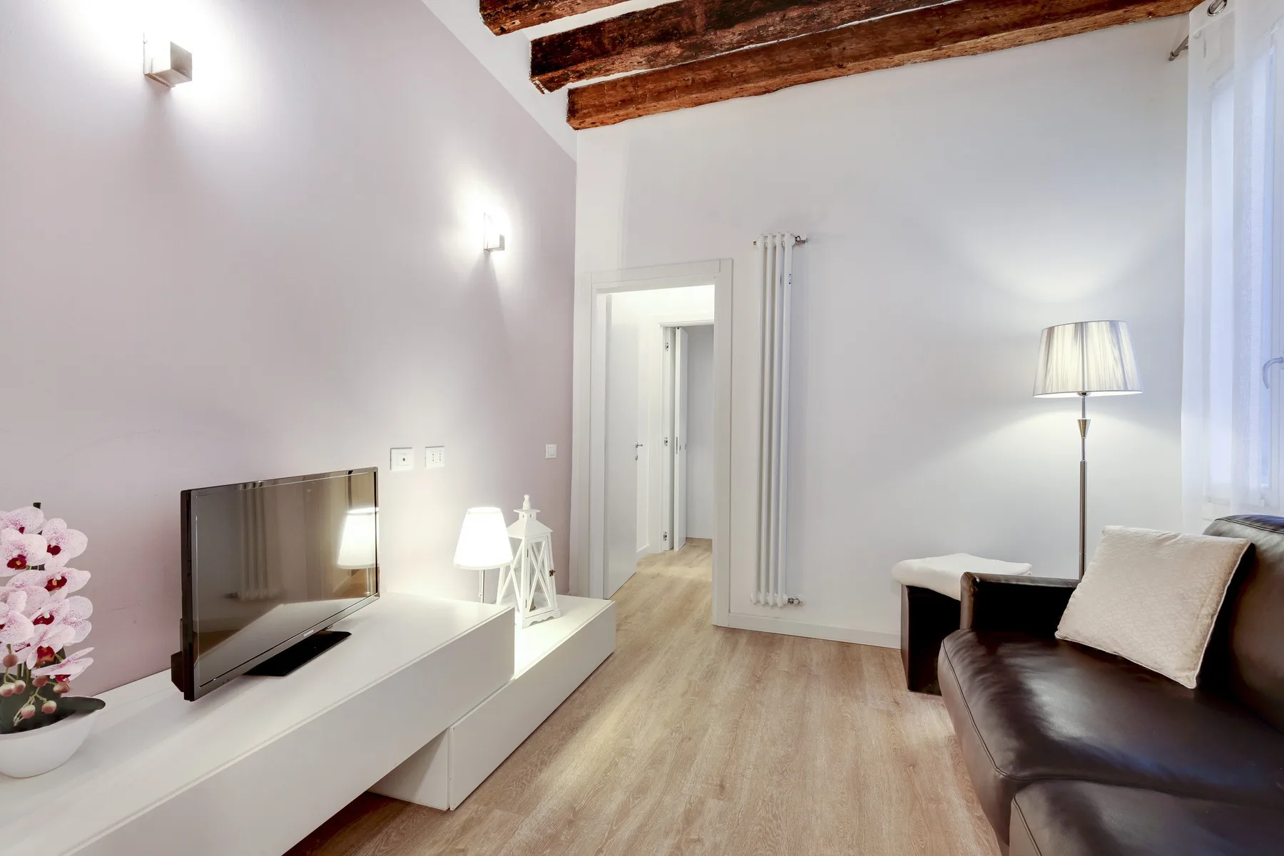 A bright living room with a television, seating, and exposed ceiling beams.