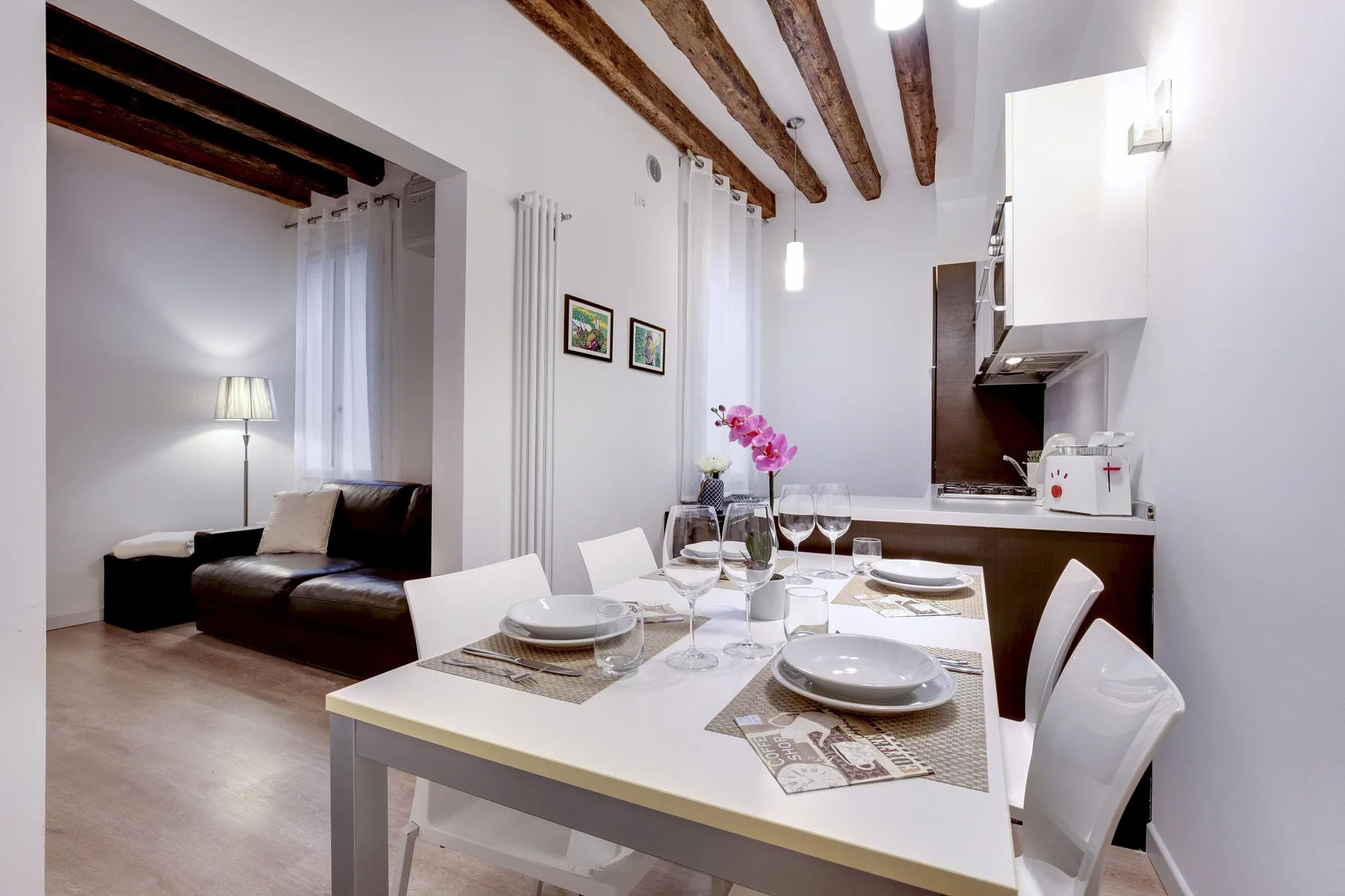 A dining table with place settings sits beside a compact kitchen and a small seating area.