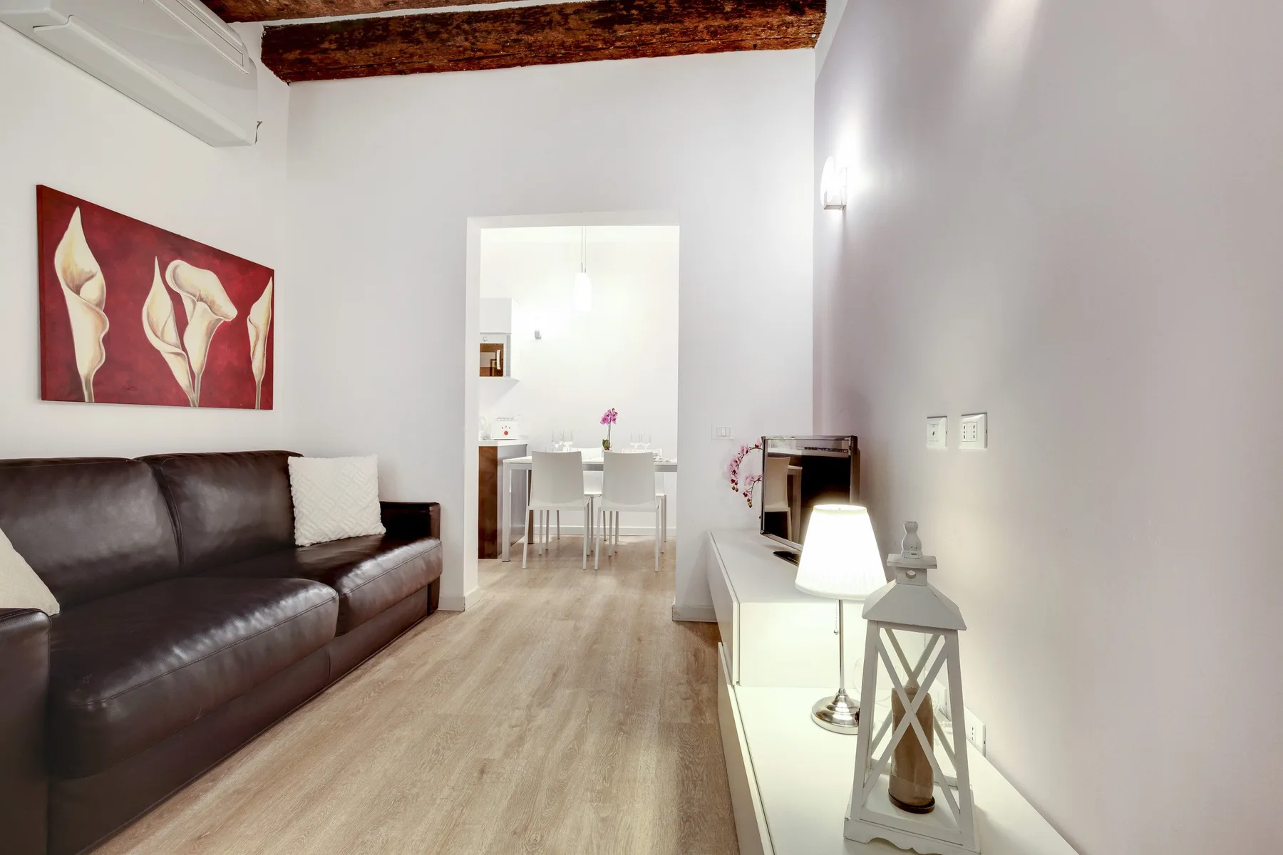 A living room with dark seating, a low console, and a dining area beyond.