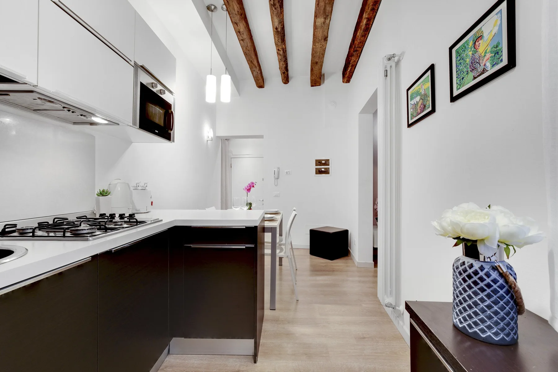 A bright kitchen with a dark counter, exposed wooden ceiling beams, and framed artwork.
