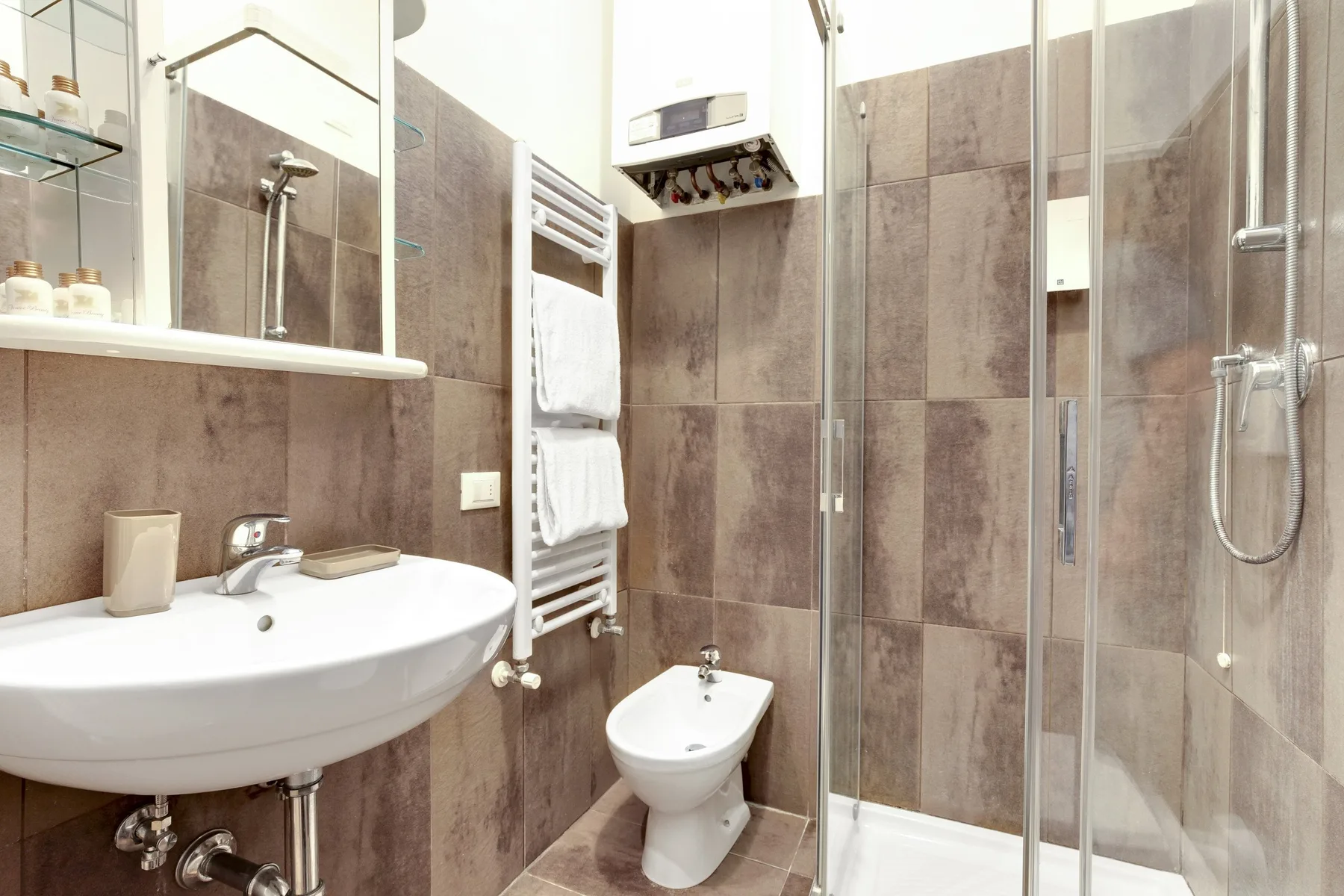 A tiled bathroom with a sink, bidet, and glass-enclosed shower.