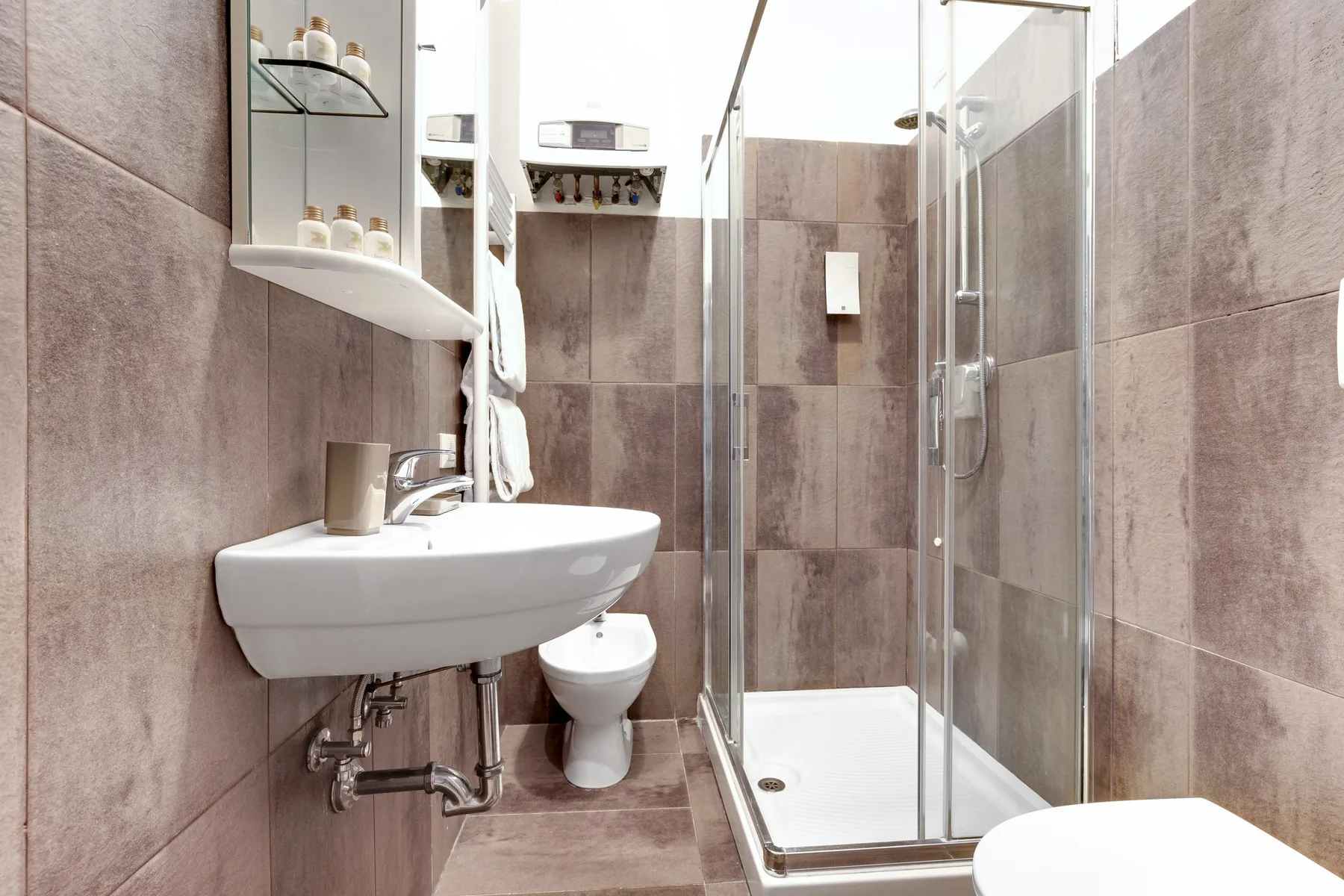 A tiled bathroom with a wall-mounted sink and glass shower.