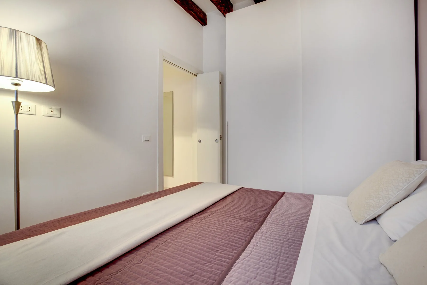 A bedroom with a neatly made bed and a floor lamp beside it.