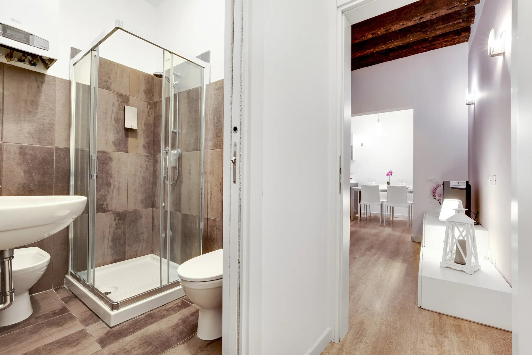 A bathroom with a glass shower and an open doorway to a dining area.
