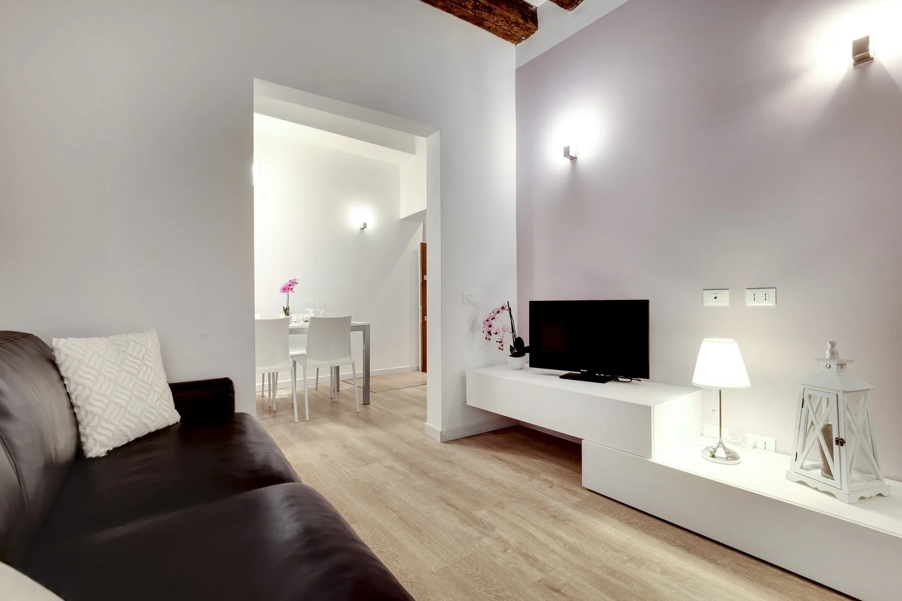 A living room with dark seating, a television, and a dining area beyond the doorway.