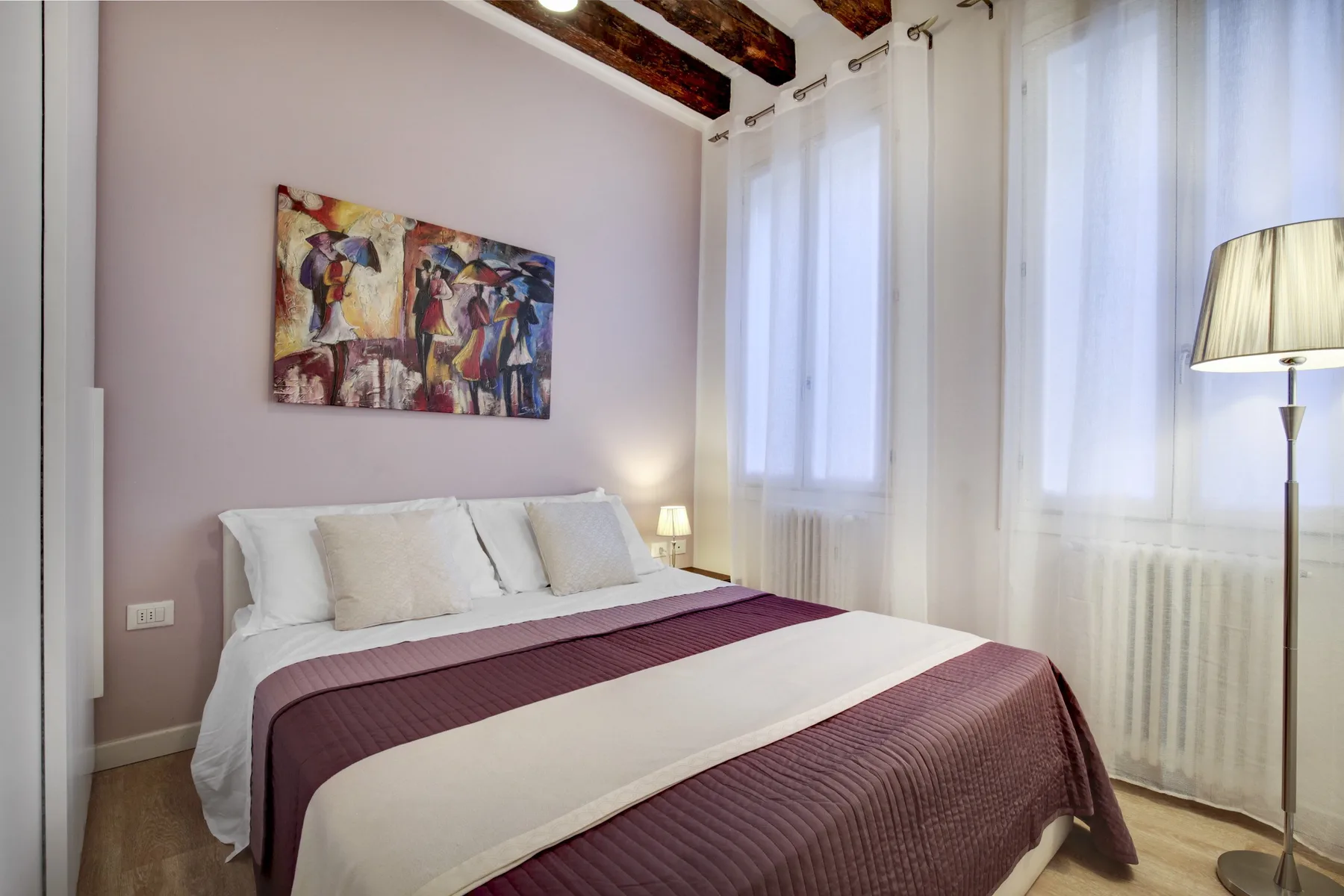 A bedroom with a neatly made bed beneath colorful wall art.