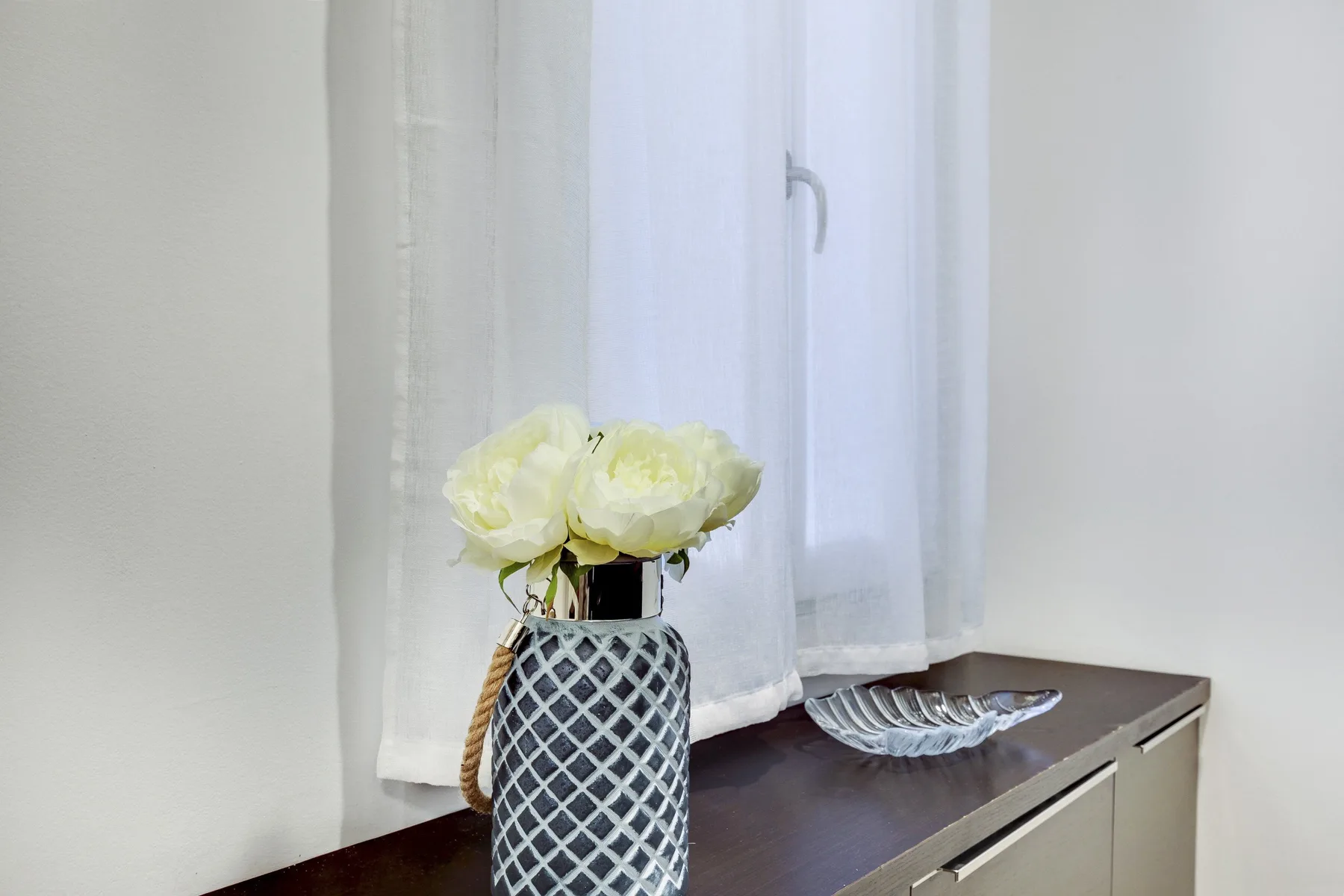 A vase of flowers sits on a dark countertop beside a window.